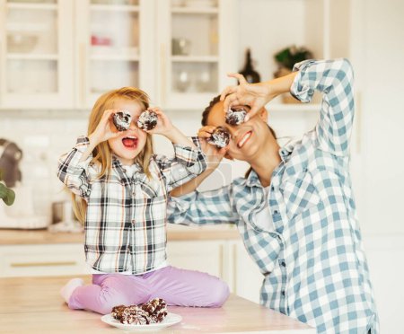 Foto de Family creativity, hobbies, joint activities with children. Mother and little daughter posing for funny portrait cook at kitchen look at camera make glasses from cookies. - Imagen libre de derechos