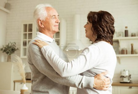 Foto de Love lives forever. The happy elderly woman and a man dancing in the kitchen. Lifestyle concept. - Imagen libre de derechos
