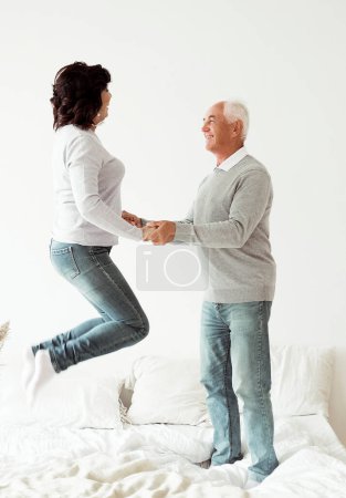 Téléchargez les photos : Senior couple at home. Handsome old man and attractive old woman are having fun and jumping in bed. Lifestyle cocnept. - en image libre de droit