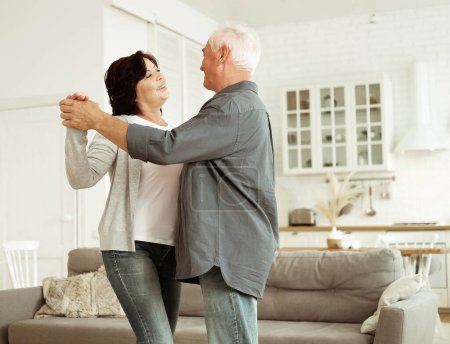 Téléchargez les photos : Carefree happy active old senior couple dancing in kitchen, cheerful retired elder husband holding hand of mature middle aged wife enjoy fun leisure retirement lifestyle at home - en image libre de droit