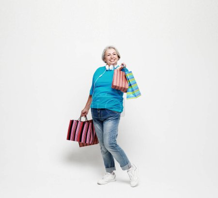 Téléchargez les photos : Full length photo of positive cheerful grey white hair elderly woman enjoy leisure time shopping hold bags wear jeans and blue shirt isolated over white background - en image libre de droit