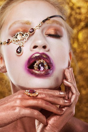 Photo for Charming young woman model holding a precious ring in her mouth. Bright makeup, gold on the lips. - Royalty Free Image