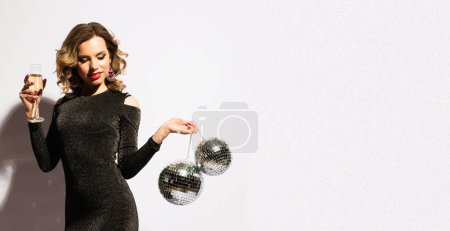Foto de Navidad, fiesta de celebración, concepto de vacaciones. Mujer joven en vestido de noche con champán y bola de discoteca. Maquillaje brillante y peinado ondulado. - Imagen libre de derechos