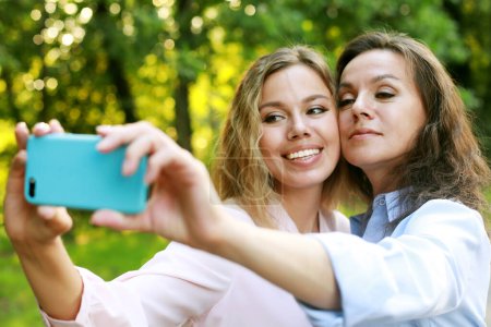 Foto de Concepto de estilo de vida, familia y personas: la madre madura y la hija adulta están haciendo selfie por teléfono móvil en el parque de verano - Imagen libre de derechos