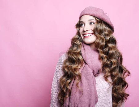 Foto de Beautiful young woman with long wavy hair wearing pink beret and scarf over pink background - Imagen libre de derechos