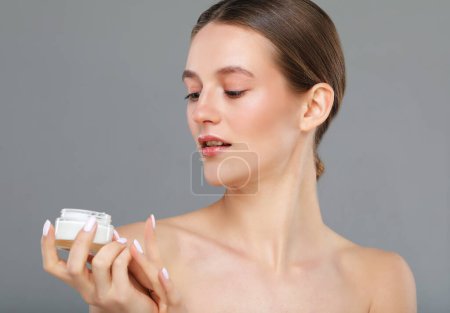 Téléchargez les photos : Concept of using moisturizing cream before going to bed. Beautiful cute pretty charming woman is holding a cream jar isolated on grey color background - en image libre de droit
