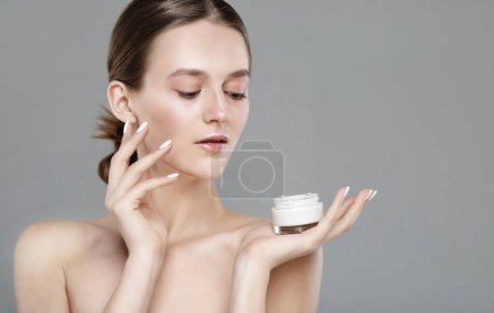 Foto de Concept of using moisturizing cream before going to bed. Beautiful cute pretty charming woman is holding a cream jar isolated on grey color background - Imagen libre de derechos