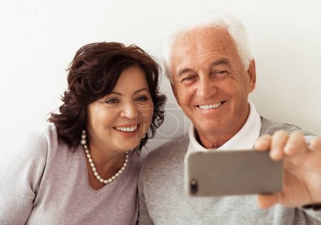 Téléchargez les photos : Famille, technologie, âge, geste et concept de personnes - heureux couple de personnes âgées avec smartphone faire du selfie et saluer la main à la maison - en image libre de droit
