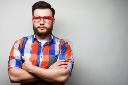 Téléchargez les photos : Portrait of bearded handsome man wearing glasses in plaid shirt crossing hands and look at camera over grey background - en image libre de droit