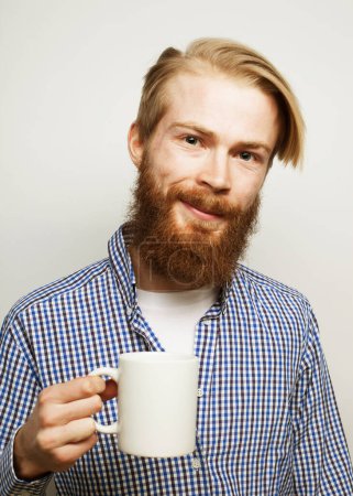 Foto de Good morning, man holding a cup tea. Morning concept. Handsome bearded male holds cup of coffee, tea. Smiling hipster man with cup of fresh coffee. Isolated over grey background. - Imagen libre de derechos