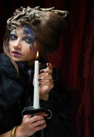 Téléchargez les photos : Belle femme dans un costume de sorcière avec un maquillage lumineux et une coiffure tient une bougie. Halloween. Fête. Vacances. Carnaval. - en image libre de droit
