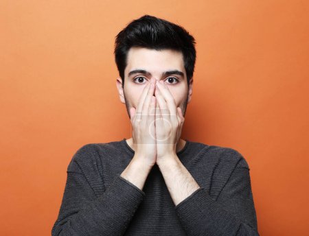 Photo for Young handsome man covers mouth with hands over orange color background - Royalty Free Image