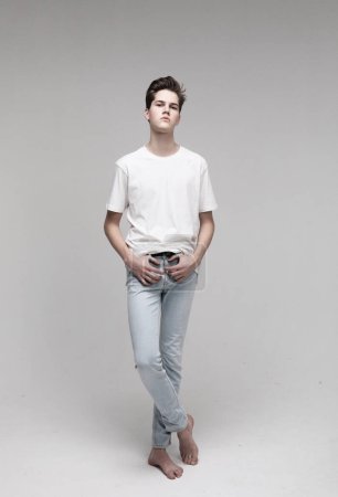 Foto de Young Male Model wearing white t-shirt and jeans. Portrait over grey background. - Imagen libre de derechos