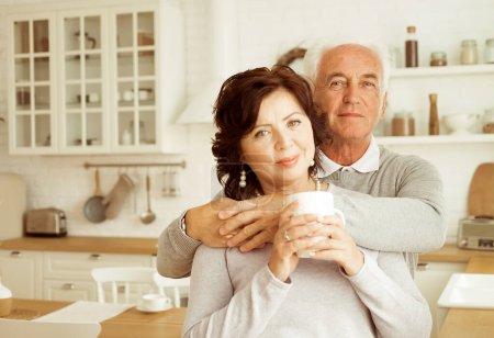 Téléchargez les photos : Happy elderly couple hugging in the kitchen at home. Love and trust. Golden Age of Retirement. - en image libre de droit