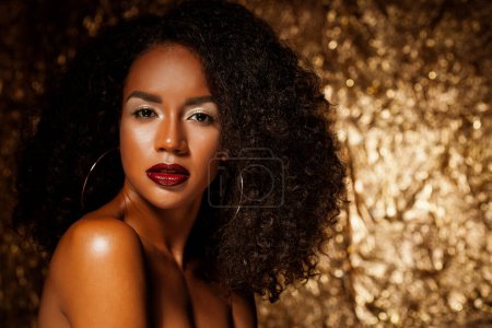 Foto de Joven mujer afroamericana hermosa con pelo afro. Maquillaje de glamour. Fondo dorado. - Imagen libre de derechos