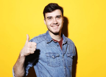 Foto de Lifestyle, body language and people concept: Happy handsome man showing thumbs up over yellow color background - Imagen libre de derechos