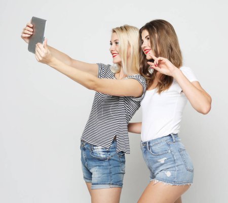 Foto de La tecnología, la amistad y el concepto de la gente - dos mujeres jóvenes sonrientes con tablet PC sobre fondo gris. - Imagen libre de derechos