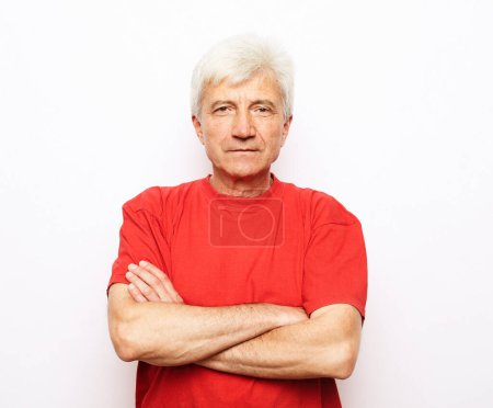 Foto de Portrait of healthy happy smile senior elderly caucasian old man wearing red t-shirt with arm crossed over white background - Imagen libre de derechos