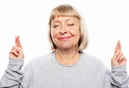 Photo for Old people, modern lifestyle, body language concept. Portrait of an elderly woman with short blond hair, fingers crossed, making a wish, daydreaming, on a white background - Royalty Free Image