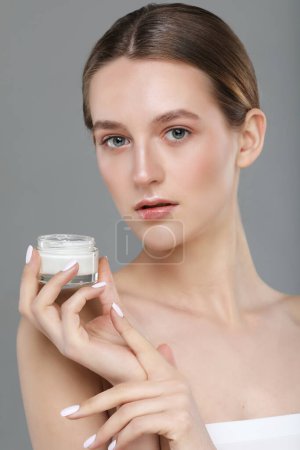 Téléchargez les photos : Concept of using moisturizing cream before going to bed. Beautiful young charming woman is holding a cream jar isolated on grey background - en image libre de droit