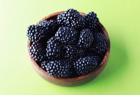 Photo for Blackberries in a wooden bowl. Ripe and tasty black berry isolated on green baclground. Close up. - Royalty Free Image