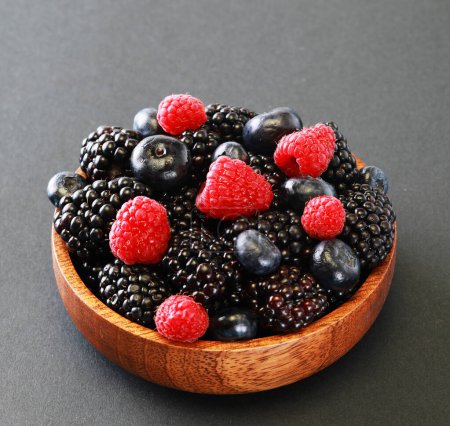 Téléchargez les photos : Blackberries, raspberry and blueberrys in a wooden bowl. Ripe and tasty black berry isolated on grey baclground. Close up. - en image libre de droit