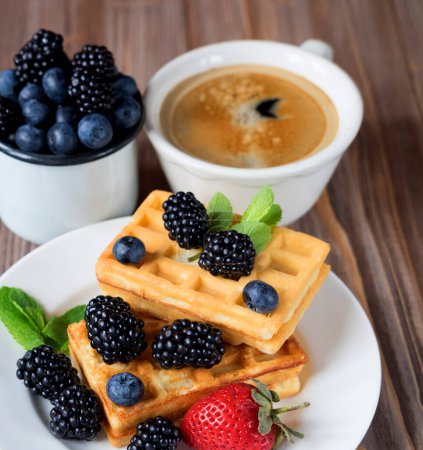 Téléchargez les photos : Good morning. Waffles with blueberries, strawberry and blackberries with a cup of coffee for breakfast over wooden table. - en image libre de droit