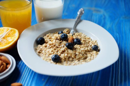 Photo for Healthy breakfast, food and diet concept - oatmeal with fresh berries on white plate with orange juice and milk, blue wooden background. - Royalty Free Image