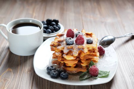 Belgian waffles with fresh berries amd a cup of coffee over wooden background, close up