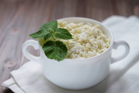 Foto de Good breakfast. Cottage cheese with mint in a white bowl on a white napkin. - Imagen libre de derechos