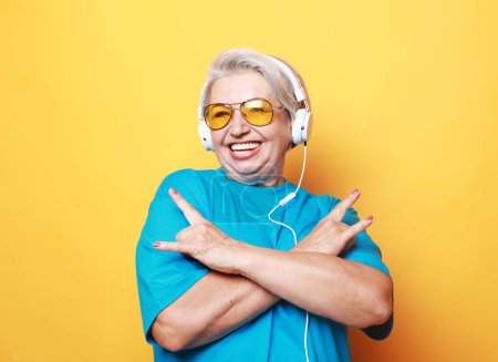 Photo for Music lover. Funny old lady listening music and showing thumbs up, yellow background, - Royalty Free Image