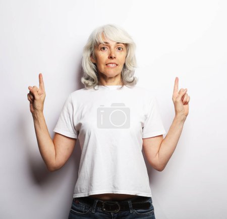 Téléchargez les photos : Smiling elderly gray-haired woman lady 60s years old pointing index finger aside up over grey background - en image libre de droit