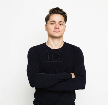 Photo for Waist-up shot of young man wearing black sweater looking at camera with crossed arms over white background - Royalty Free Image