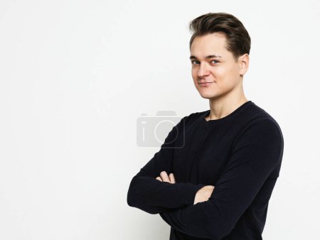 Foto de Joven hombre guapo con suéter negro cruzando las manos y mirar a la cámara sobre fondo blanco - Imagen libre de derechos