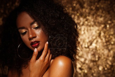 Téléchargez les photos : Beautiful young African woman with bright make up posing against a gold background. - en image libre de droit