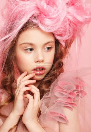 Photo for Little child girl in a pink dress, like a princess, pink hair and makeup. Close up portrait over pink background. - Royalty Free Image