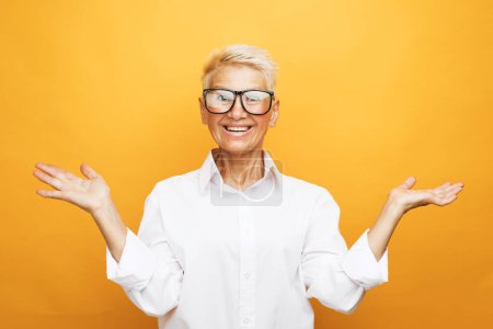 Foto de Old people, modern lifestyle, body language concept. Close-up portrait of shocked mature woman with short white hair, looking at camera, isolated on yellow background - Imagen libre de derechos