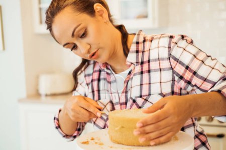 Téléchargez les photos : Beautiful young woman cuts cake cakes with a knife on the kitchen, - en image libre de droit