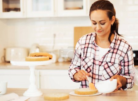 Téléchargez les photos : A young woman chef smears a cake with strawberry jam. Home business. Hobby. - en image libre de droit