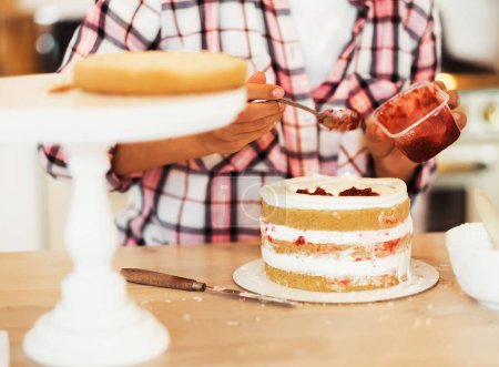 Photo for A young woman chef smears a cake with strawberry jam. Home business. Hobby. - Royalty Free Image
