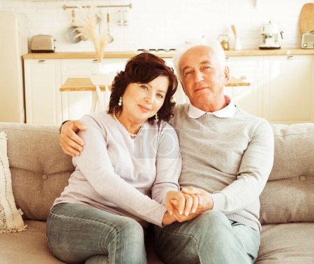 Téléchargez les photos : Mature 60 year old couple hugging while sitting on sofa. Love forever. Happy family. - en image libre de droit