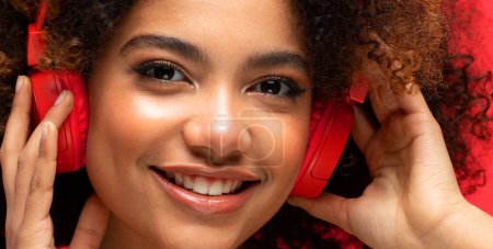 Foto de People, music, emotions concept. Young afro american female with dances in rhythm of melody, listens loud song in headphones over red background. - Imagen libre de derechos