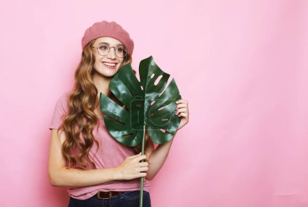 Téléchargez les photos : Beautiful young woman holding a leaf of a large tropical flower over pink background - en image libre de droit