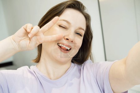 Foto de Good mood woman with expansive smile taking selfie on mobile phone at home. Lifestyle concept. - Imagen libre de derechos