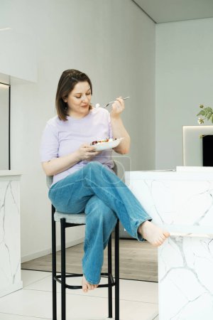 Photo for Pretty plump woman sits in the kitchen and eats salad. Lifestyle concept. - Royalty Free Image