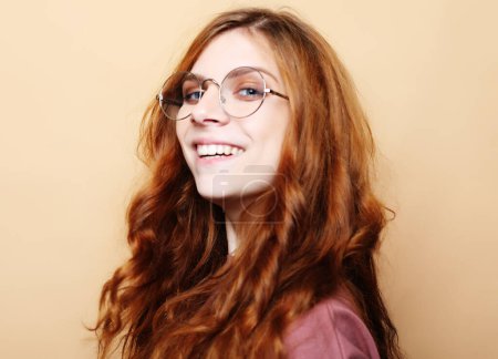 Photo for Lifestyle, emotion and body language concept: Pretty young ginger woman with curly hair and cute smile poses alone against beige background. - Royalty Free Image