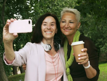 Photo for Two beautiful old women laughing in the park together on the summer day, take selfiee and feeling so happy. Lifestyle and gold age concept. - Royalty Free Image