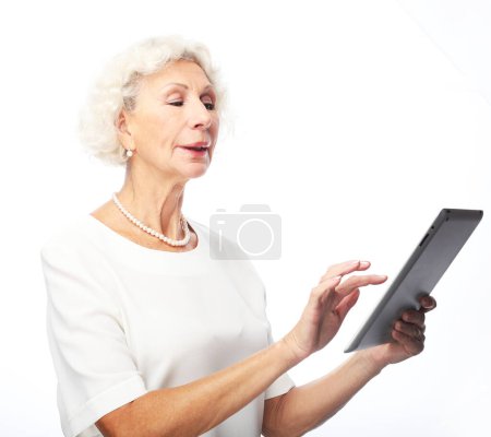 Foto de Estilo de vida, la tecnología y el concepto de las personas mayores: Mujer madura feliz con vestido blanco usando una tableta sobre fondo blanco - Imagen libre de derechos