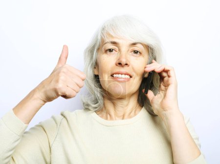 Téléchargez les photos : Modern lifestyle, tehnology and old people concept: Photo of old woman use smartphone and show thumb up isolated over white background - en image libre de droit