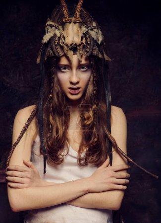 Téléchargez les photos : Jeune femme avec un maquillage lumineux, des tresses et un crâne sur la tête se tient avec les bras croisés sur un fond noir - en image libre de droit